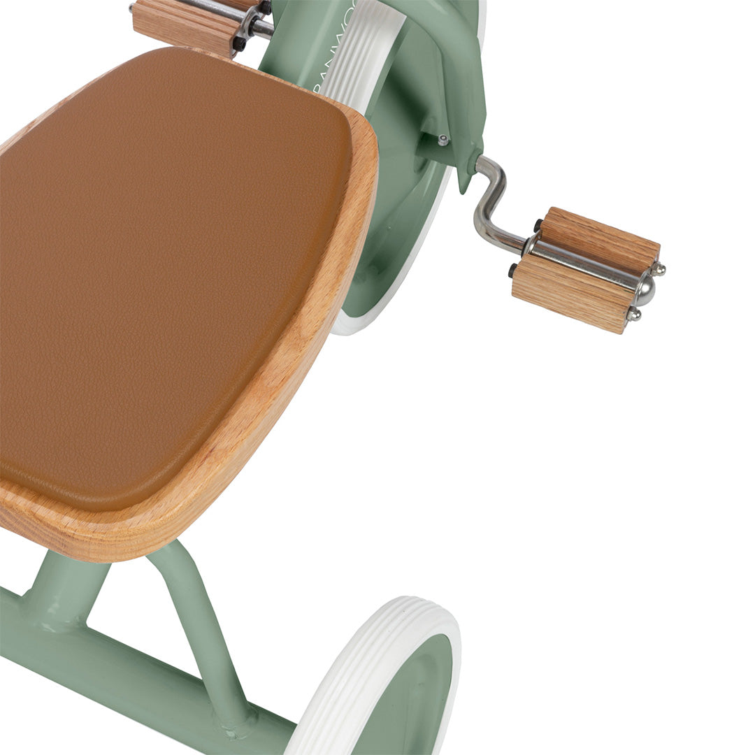 Detail van het bruine zadel en de houten pedalen van de groene Banwood driewieler.