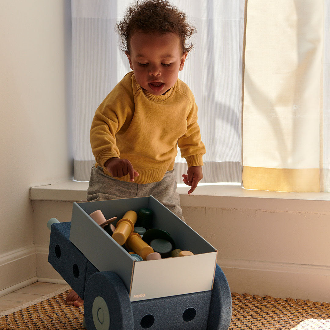 Een baby kijkt in de laadbak van de modu 3-in-1 baby walker, die is opgebouwd als een voertuig.