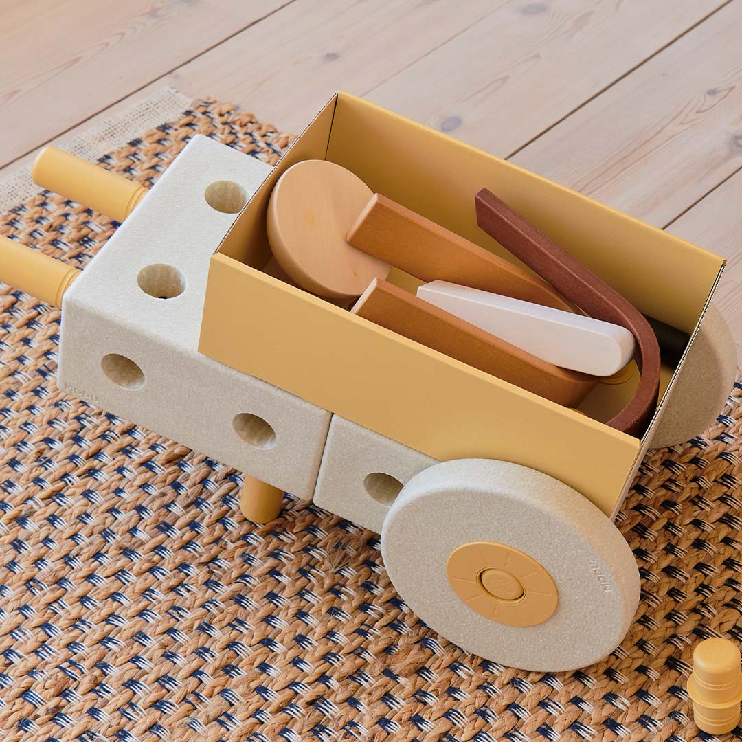 Een modu bouwwerk in de vorm van een kruiwagen, gevuld met diverse houten en plastic speelgoedonderdelen.