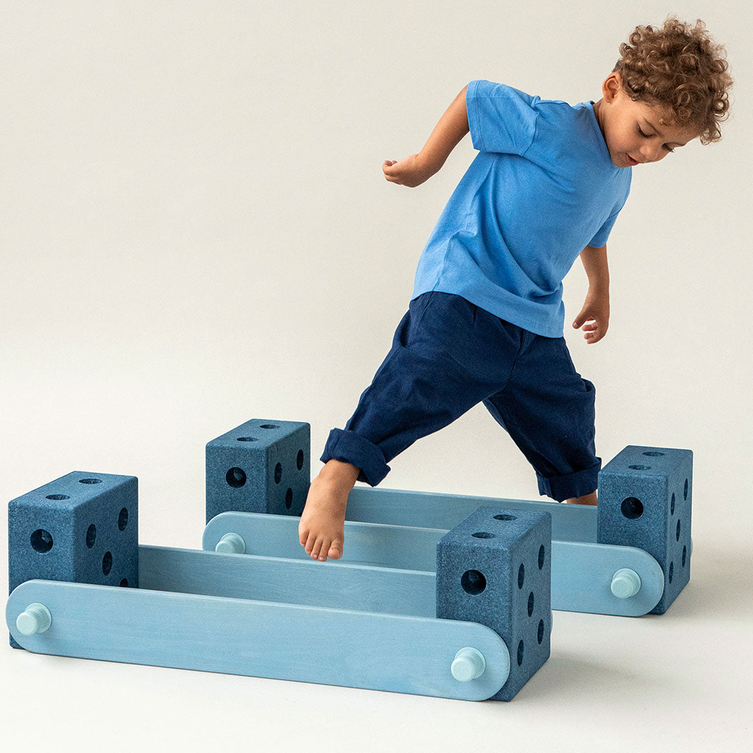 Een jongen balanceert op een speelstructuur gemaakt van diepblauwe modu schuimrubber blokken en lichtblauwe planken.