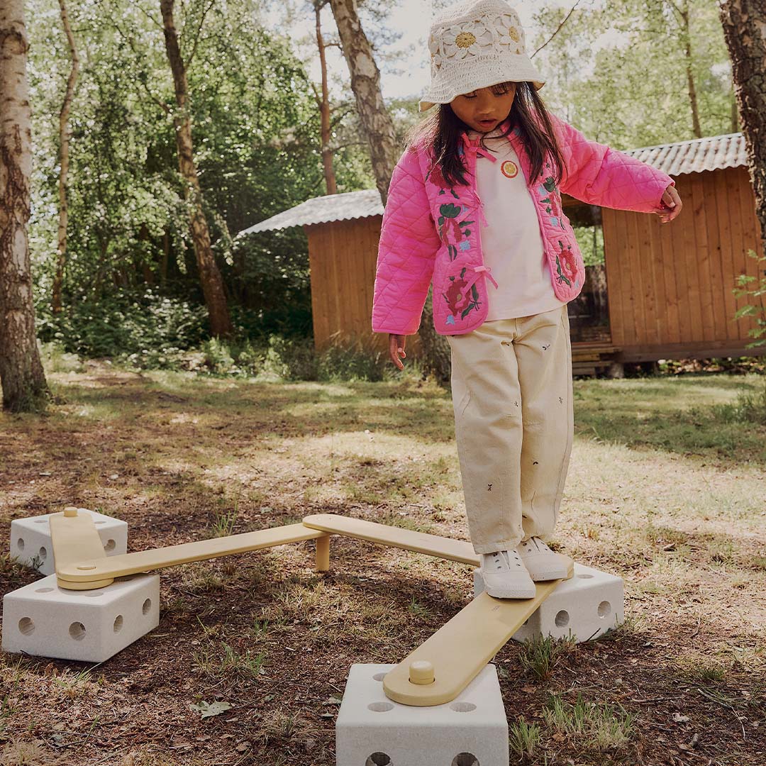 Een kind balanceert op een parcours van modu schuimrubberblokken en gele houten planken in het bos.
