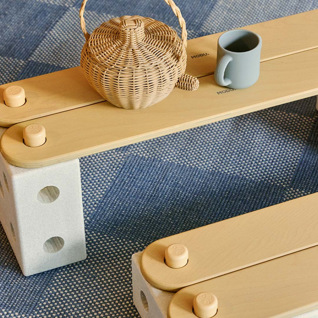 Detail van een modu honinggele evenwichtsbalk plank verbonden met een grijs blok, met een mandje en beker erop.