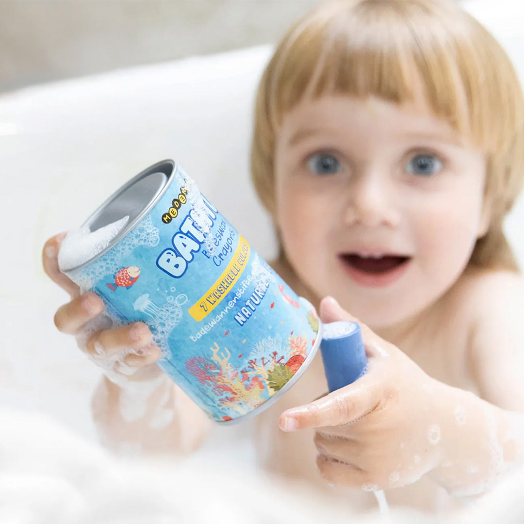Een kind in een bubbelbad houdt de Medenka badkleurkrijtjes verpakking en een blauw krijtje vast.