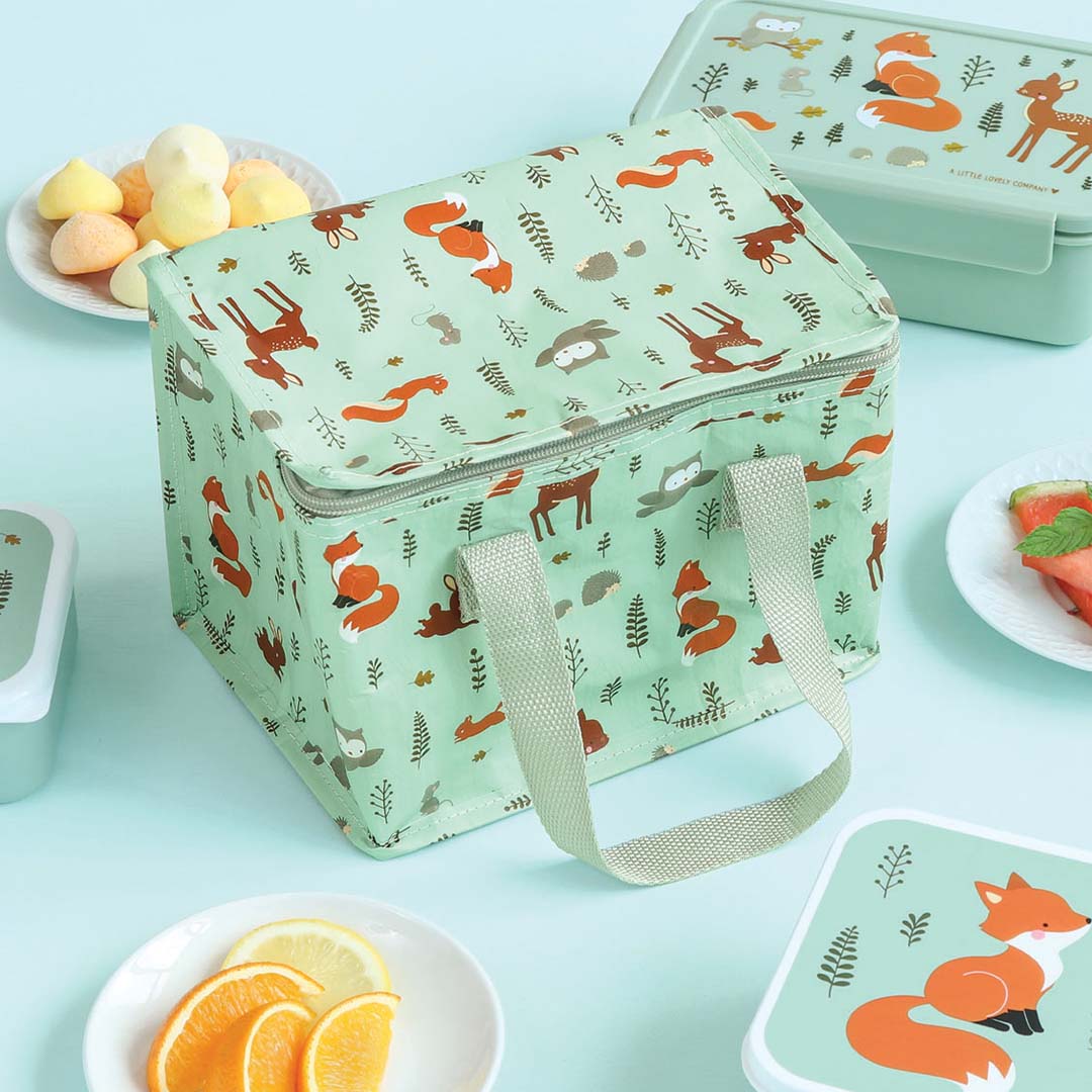 A Little Lovely Company groene koeltas met bosdierenpatroon, omringd door bijpassende lunchboxen en snacks.