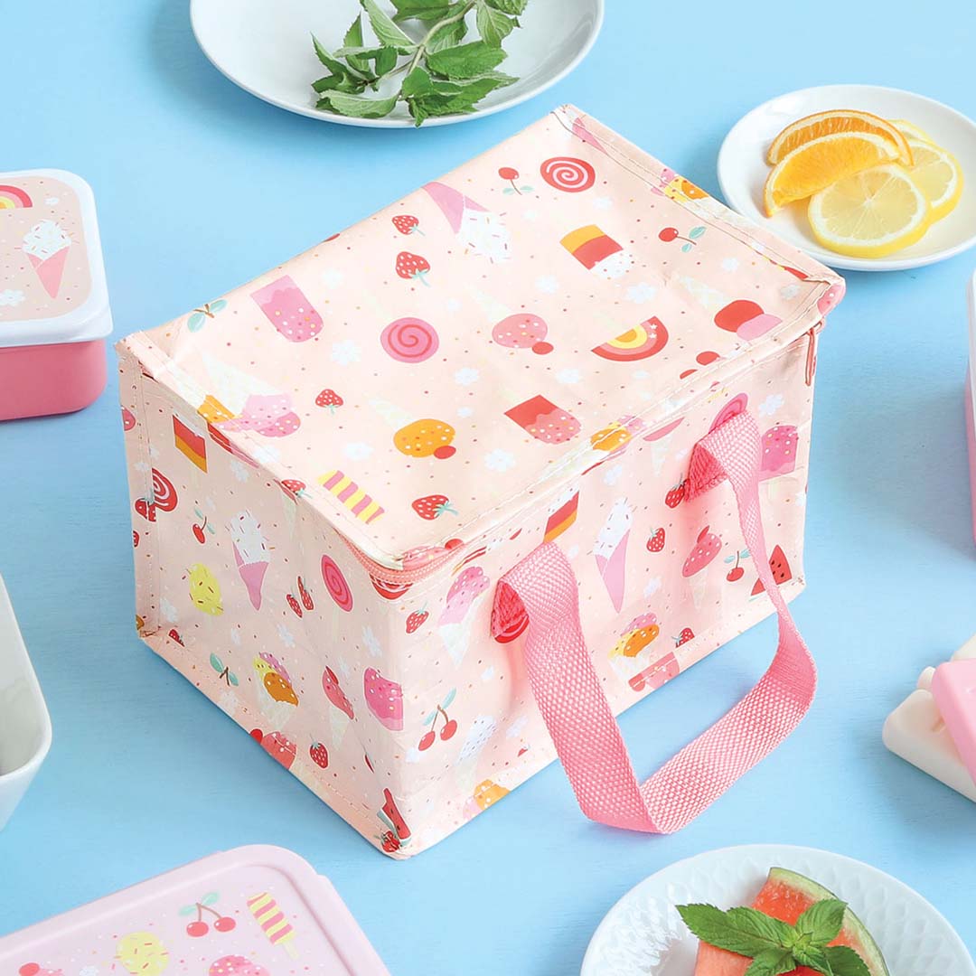 Gesloten roze koeltas met ijsjesprint op een blauwe ondergrond, omringd door fruit en lunchboxen.