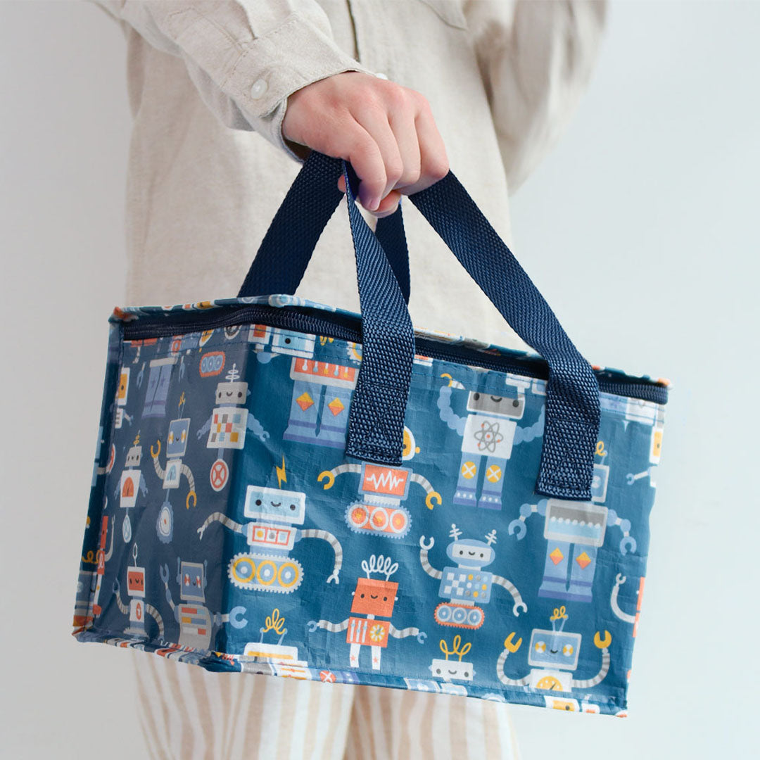 Een persoon draagt de a little lovely company koeltas met robotfiguren aan de handvatten.