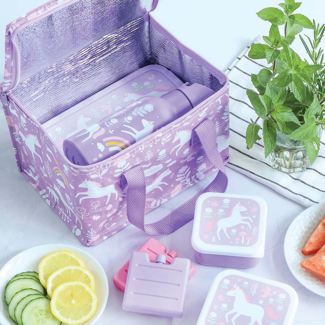 A little lovely company paarse koeltas met eenhoornpatroon open, met bijpassende lunchbox en drinkfles, omringd door fruit en koelelementen.