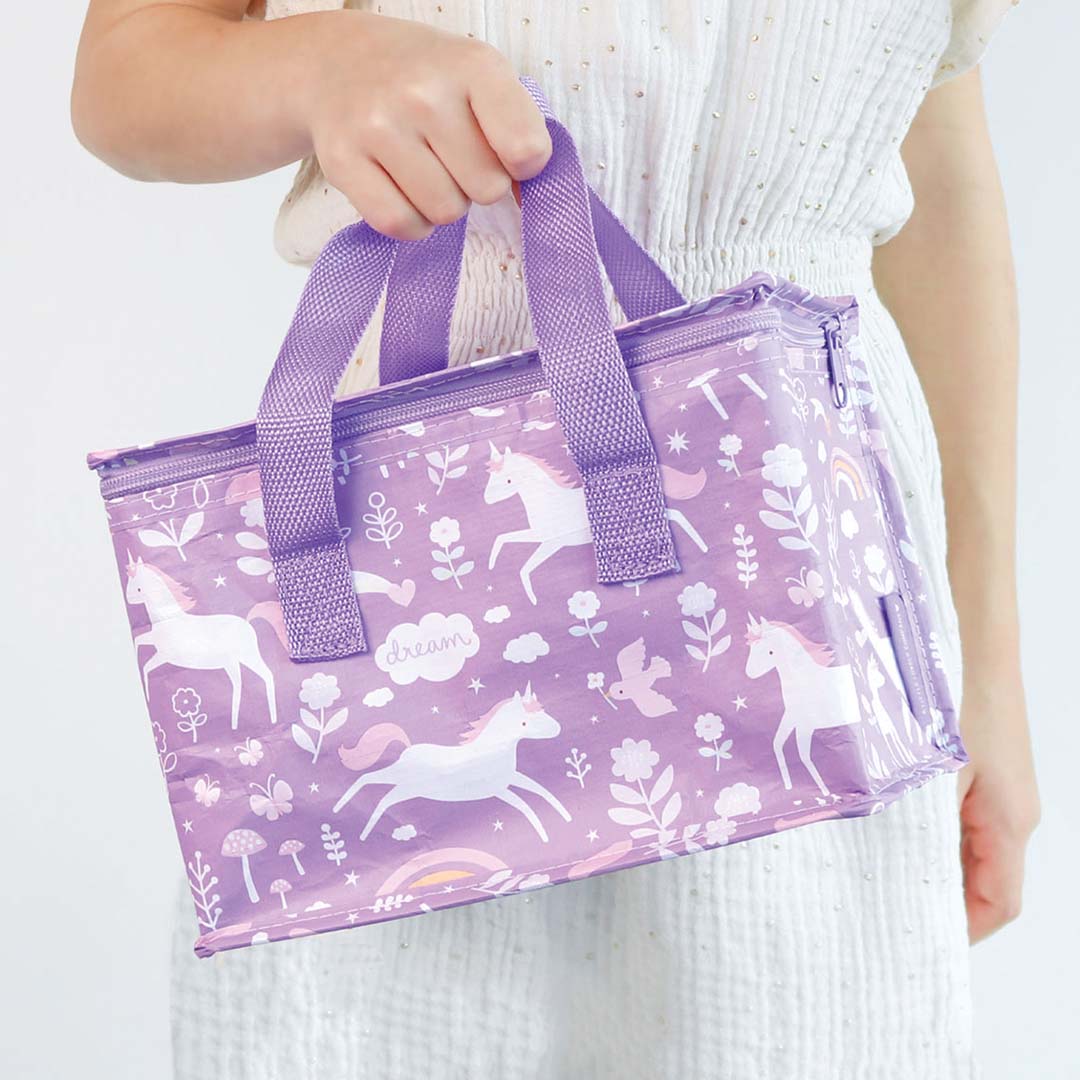 Een kind draagt de a little lovely company paarse koeltas met eenhoornpatroon aan de handvatten.