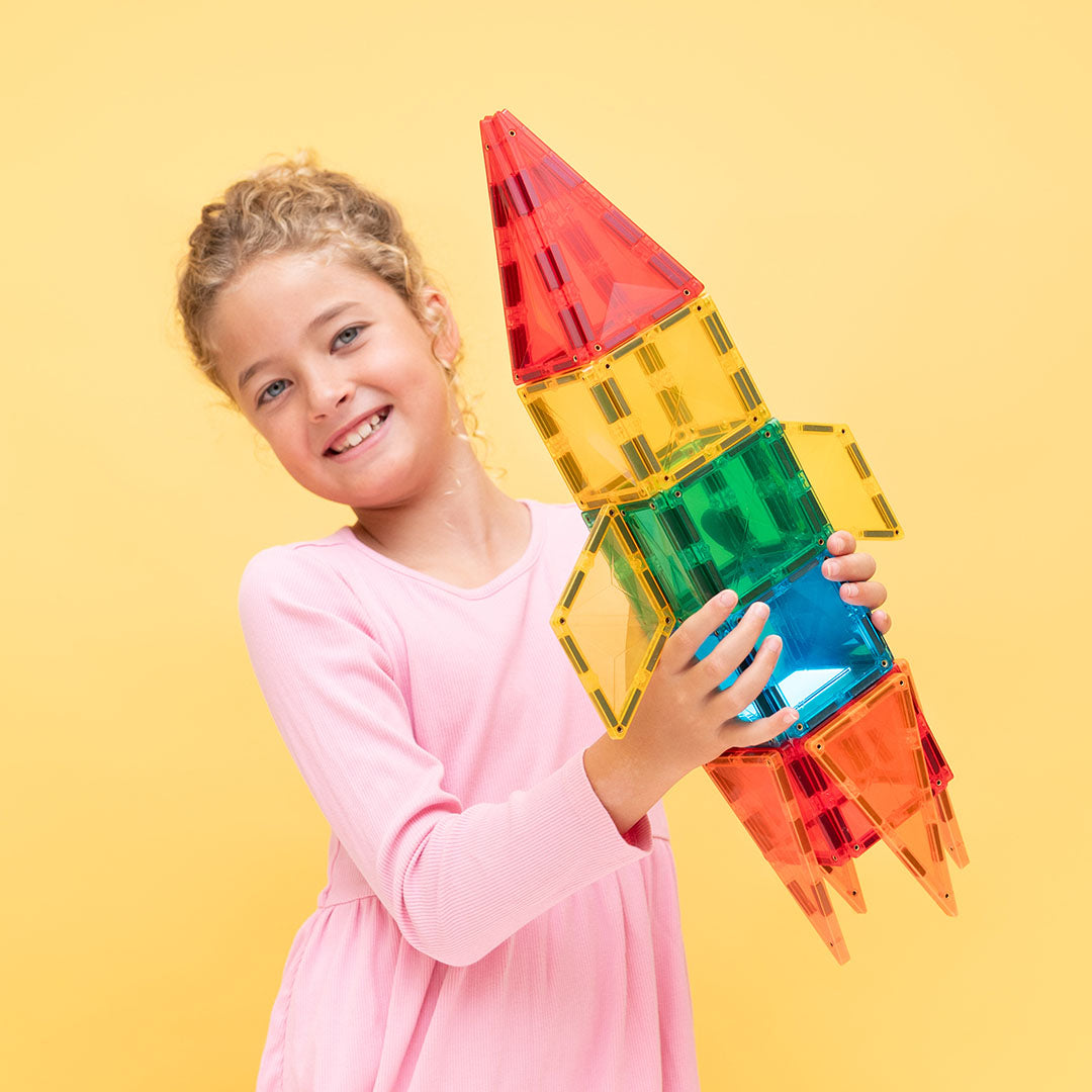 Een lachend meisje houdt een grote, kleurrijke raket vast, gemaakt van Connetix magnetische tegels.