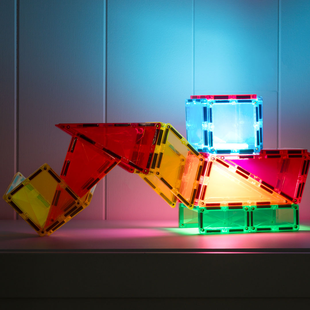 Een constructie van Connetix magnetische tegels in verschillende kleuren, waarvan sommige licht geven in een donkere omgeving.