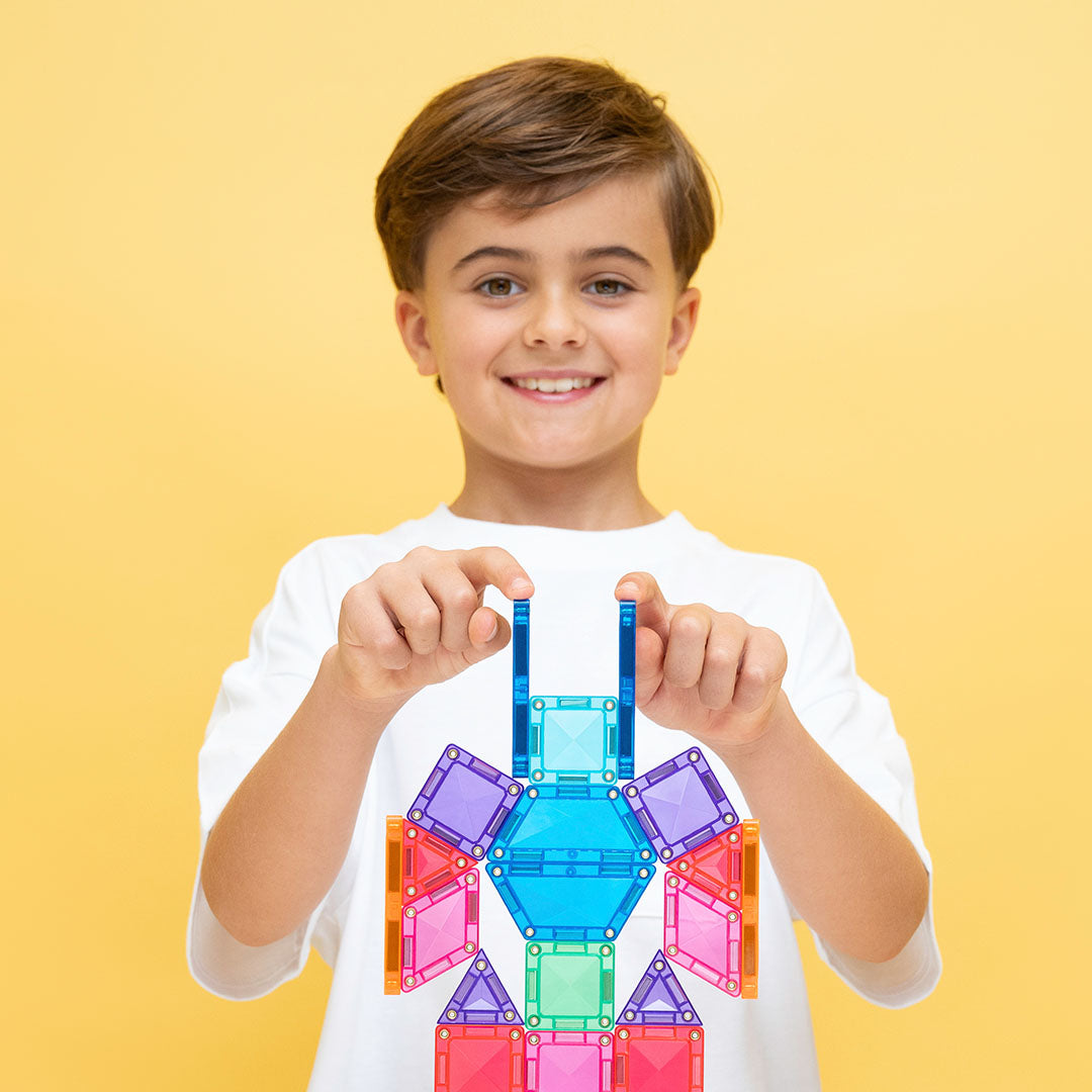 Een lachende jongen houdt een kleurrijke, abstracte vorm van Connetix magnetische tegels vast.