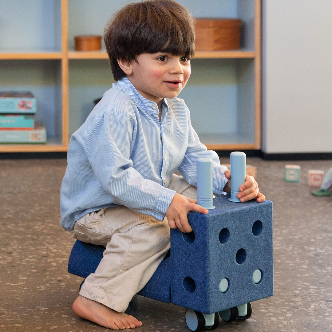 Een jongen zit op een blauwe modu bouwset constructie die als loopwagen is gebouwd.