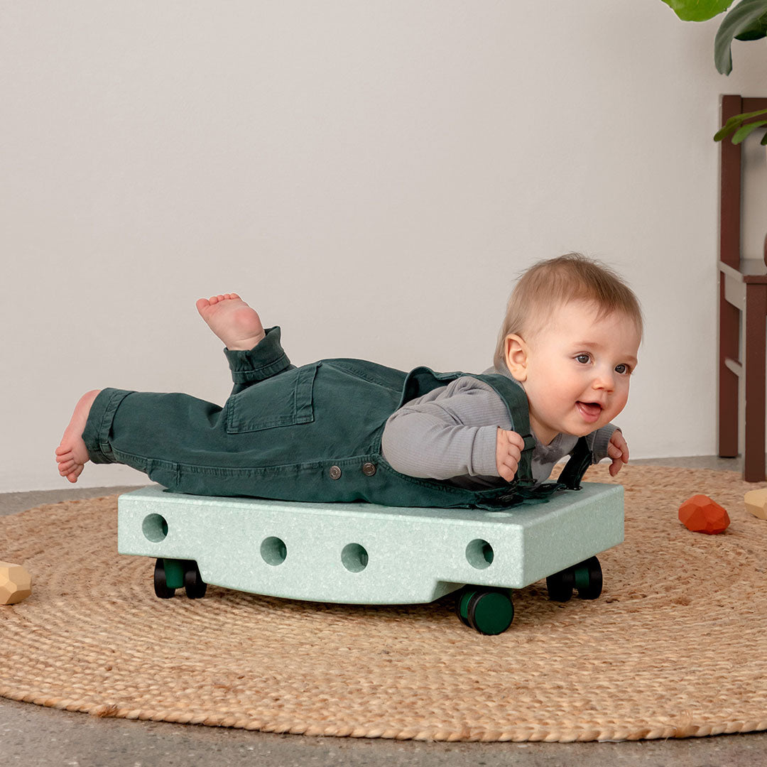 Een baby ligt lachend op de buik op een rijdend Modu schuimrubberblok in ocean mint kleur.