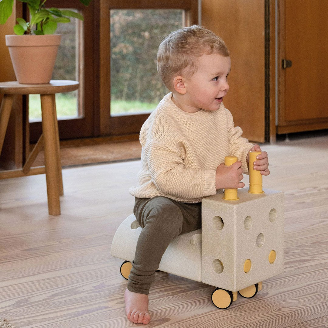 Een peuter zit op een modu bouwblok constructie met wielen, gebruikt als loopwagen.