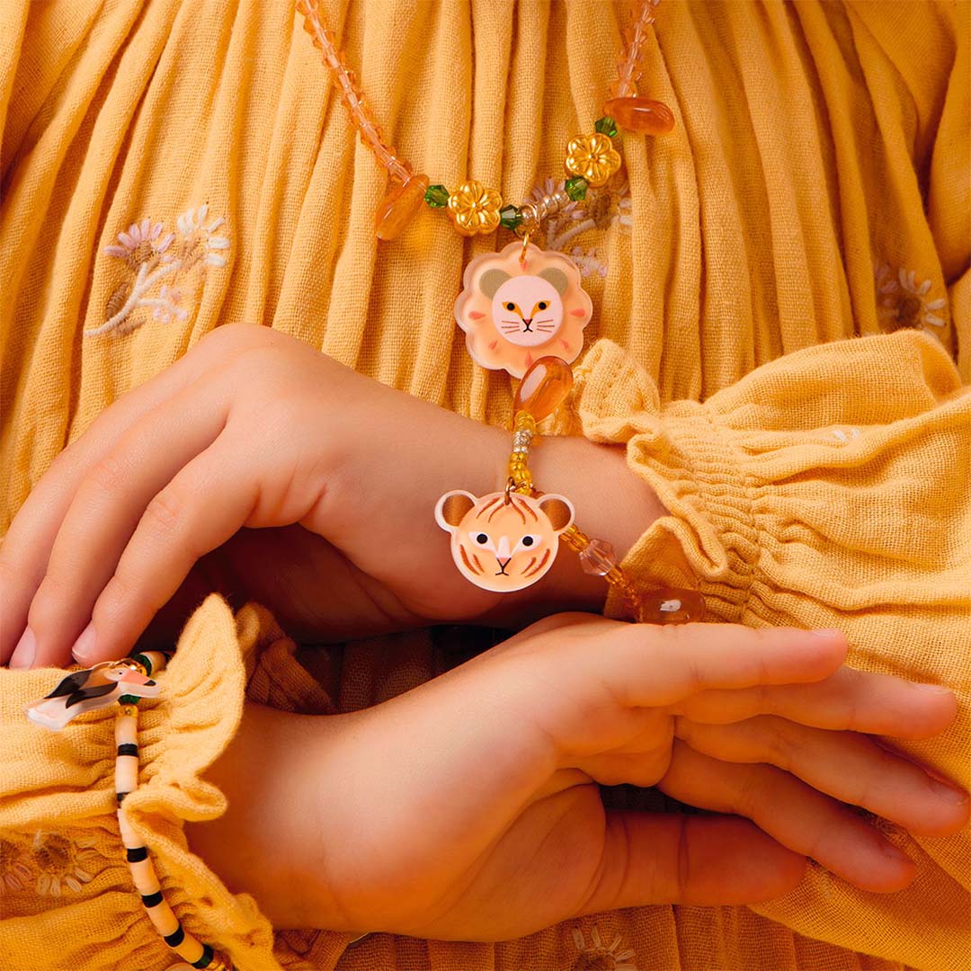 Kinderhanden dragen een Djeco kinderarmband met tijgerbedeltje en een bijpassende ketting met leeuwenbedeltje.