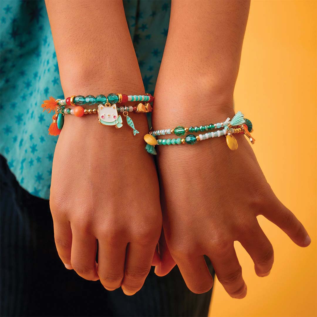 Twee kinderhanden dragen kleurrijke kralenarmbanden met bedeltjes.