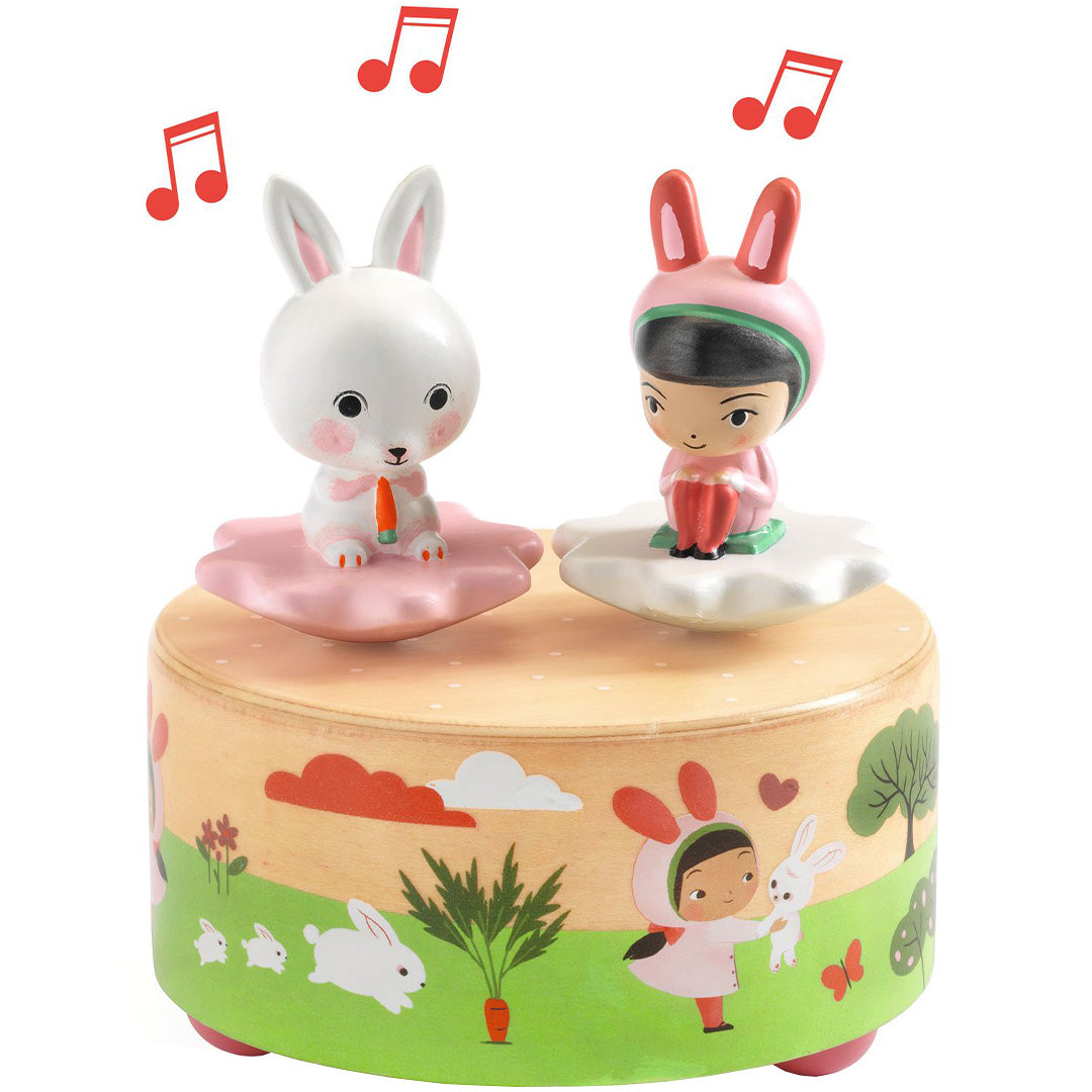 Djeco muziekdoosje met een wit konijn en een meisje in konijnenpak op een houten basis met tuindecoratie.