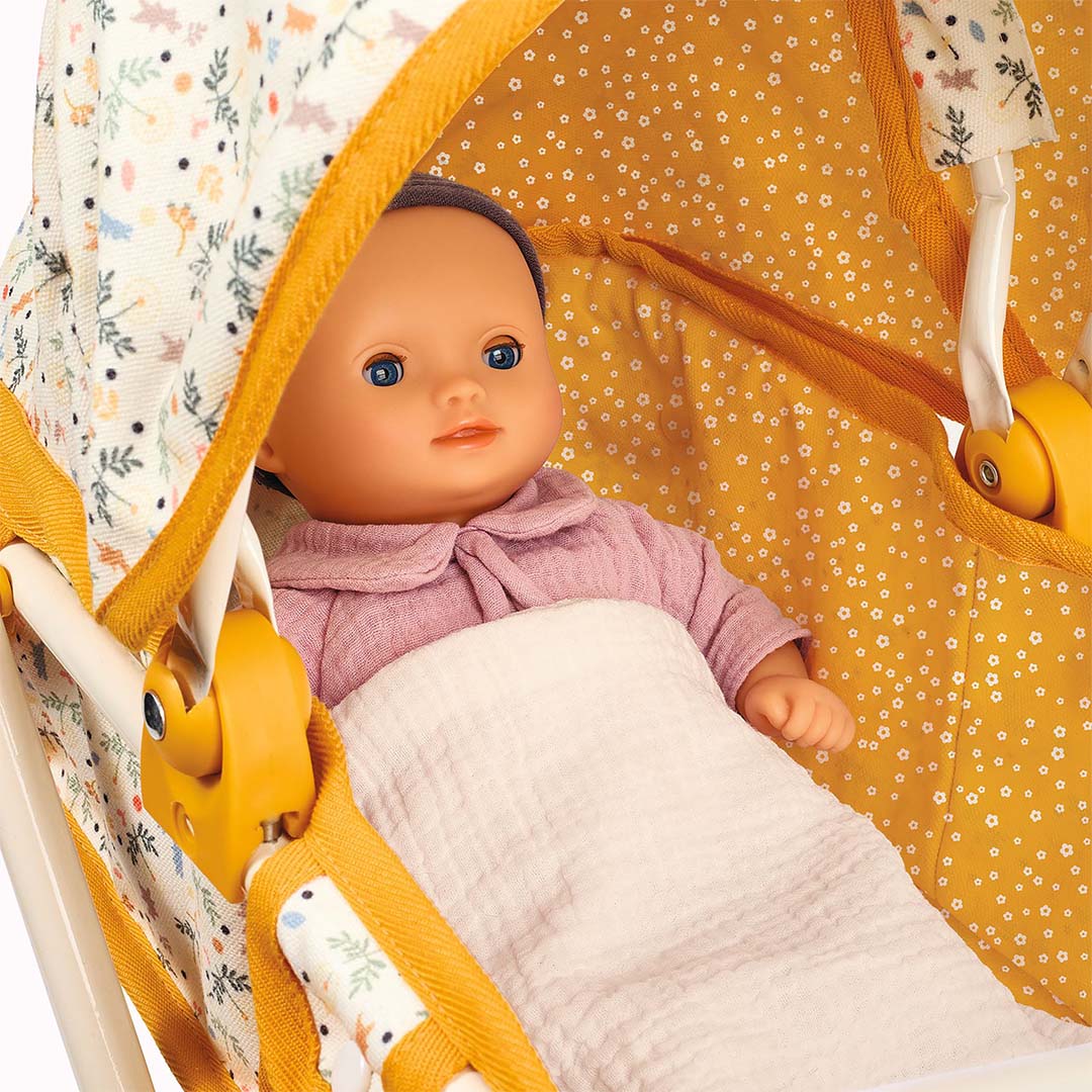 Close-up van een pop met roze kleding en deken in de Djeco poppenwagen.