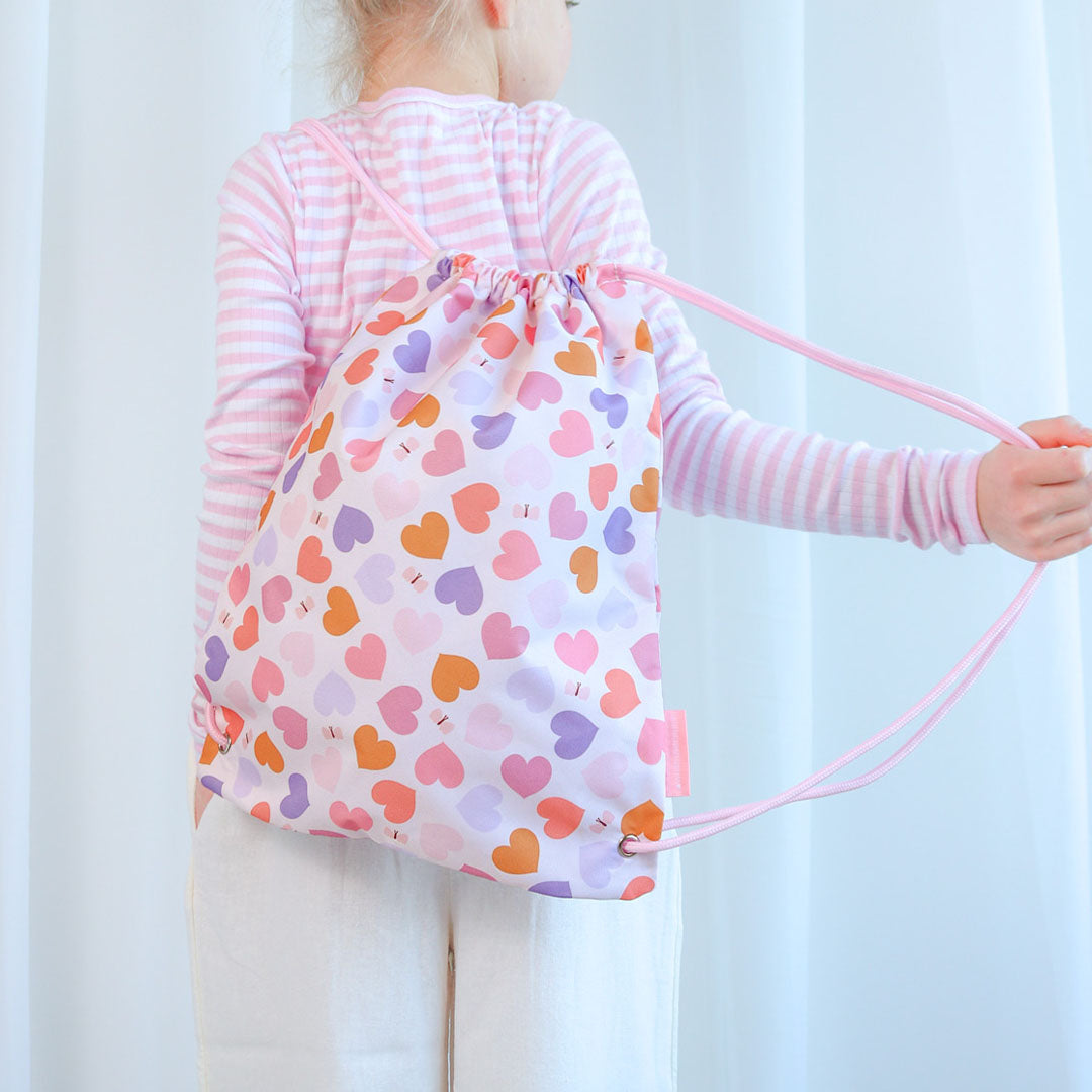 Kind draagt de a little lovely company gymtas met hartjespatroon op de rug.