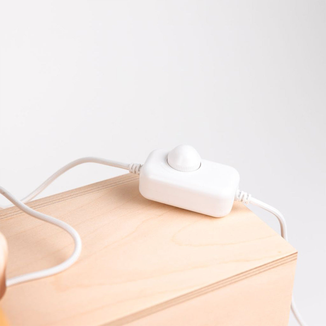 Een witte dimmer schakelaar op een wit snoer, liggend op een lichte houten ondergrond.