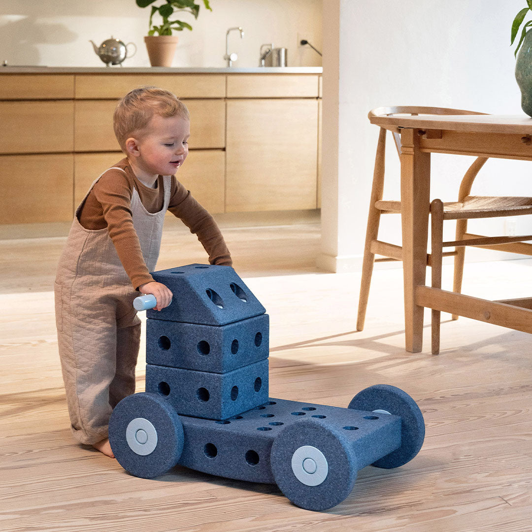 Peuter duwt een Modu blauwe schuimrubber loopwagen gemaakt van bouwblokken.