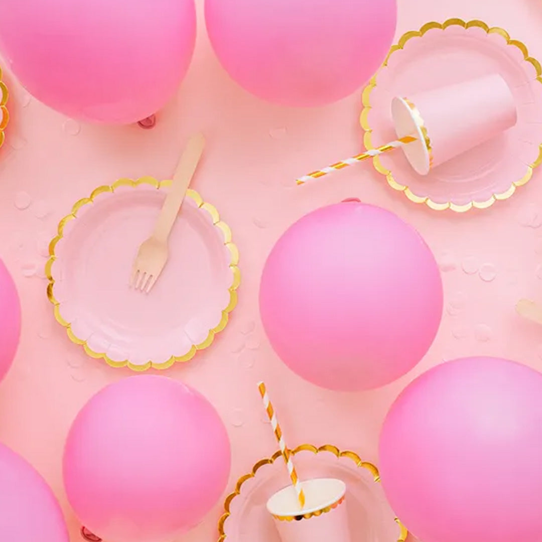 Partydeco feestdecoratie met pastel roze ballonnen, bordjes en bekers op een roze achtergrond.