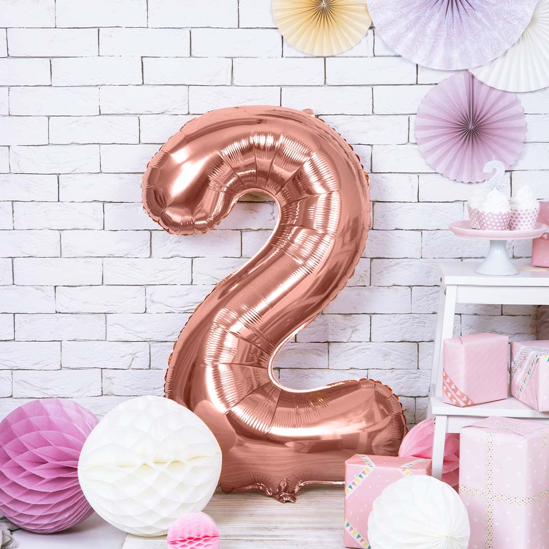 Rosegouden cijferballon 2 in een feestelijke setting met roze en witte decoraties en cadeaus.