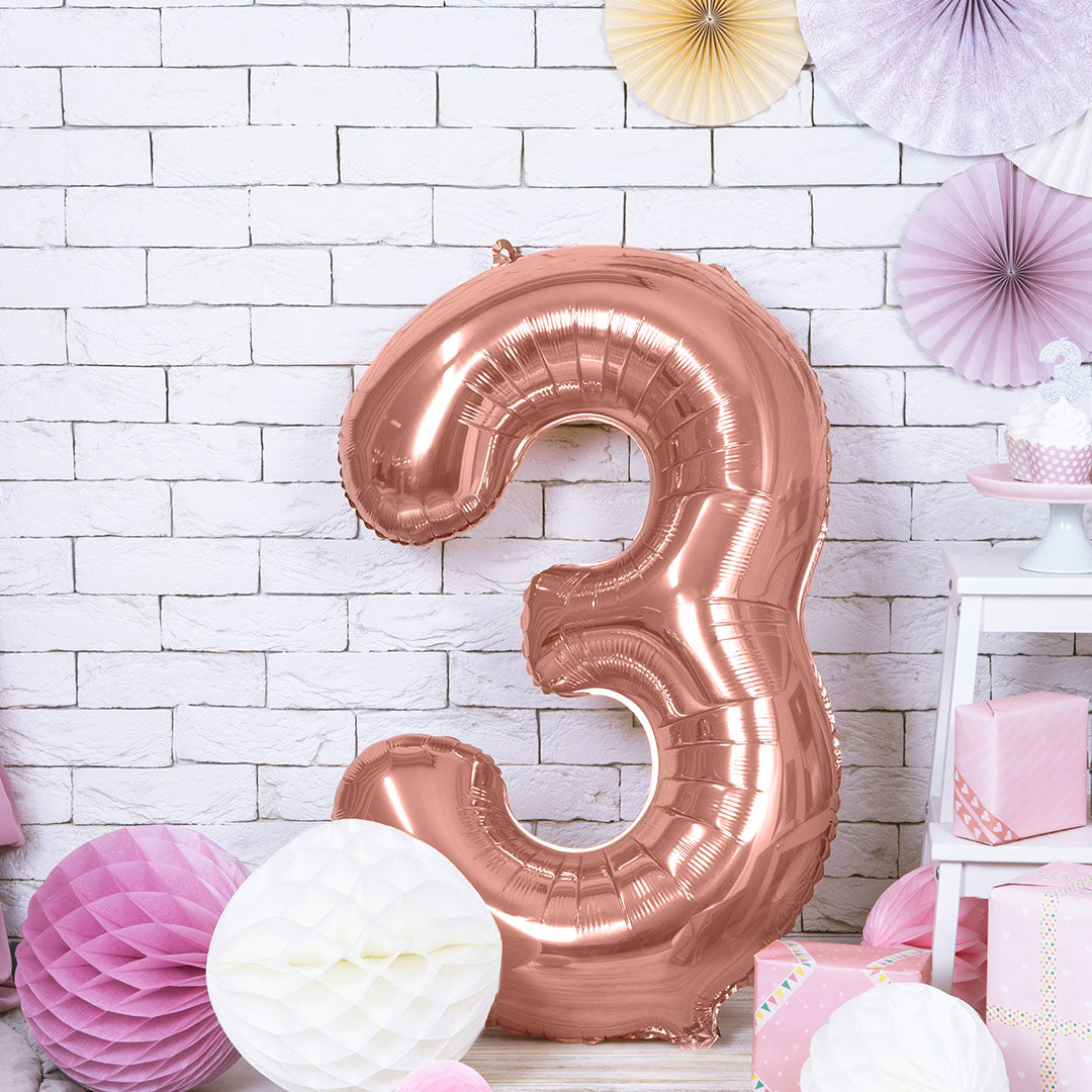 Grote roségouden cijferballon 3 als feestdecoratie in een kamer met roze en witte versieringen.