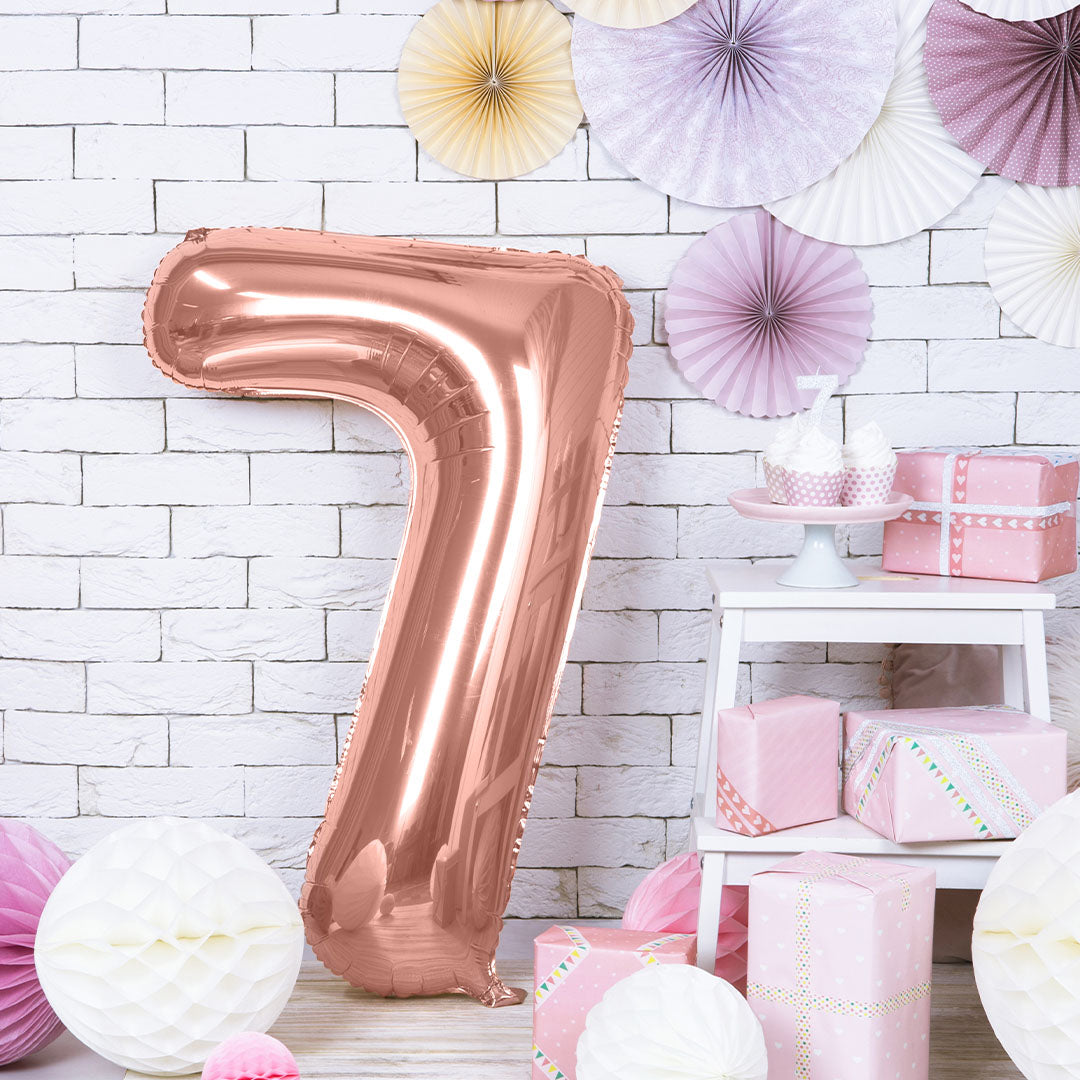 Roségouden cijferballon nummer 7 als feestdecoratie in een kamer met cadeaus en papieren waaiers.