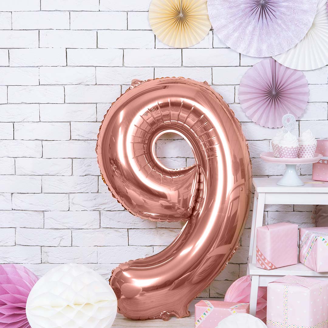 Roségouden cijferballon 9 als feestdecoratie in een kamer met roze geschenken en papieren waaiers.