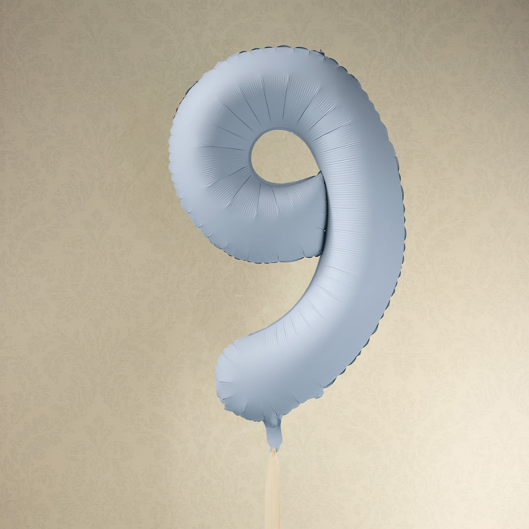 Partydeco cijferballon 9 in misty blauw zwevend voor een lichtbeige muur.
