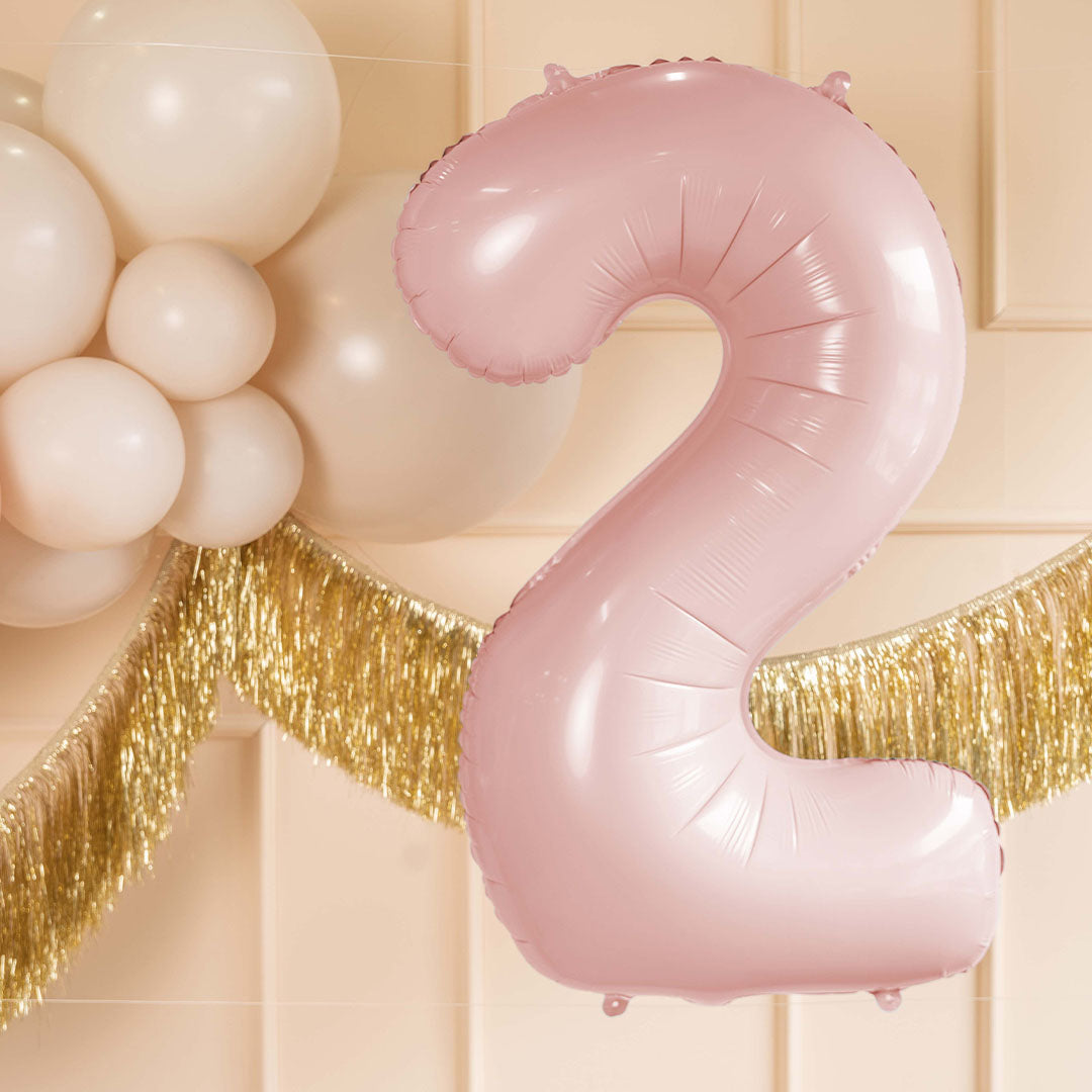 Partydeco lichtroze cijferballon '2' hangend tussen witte ballonnen en een gouden slinger.