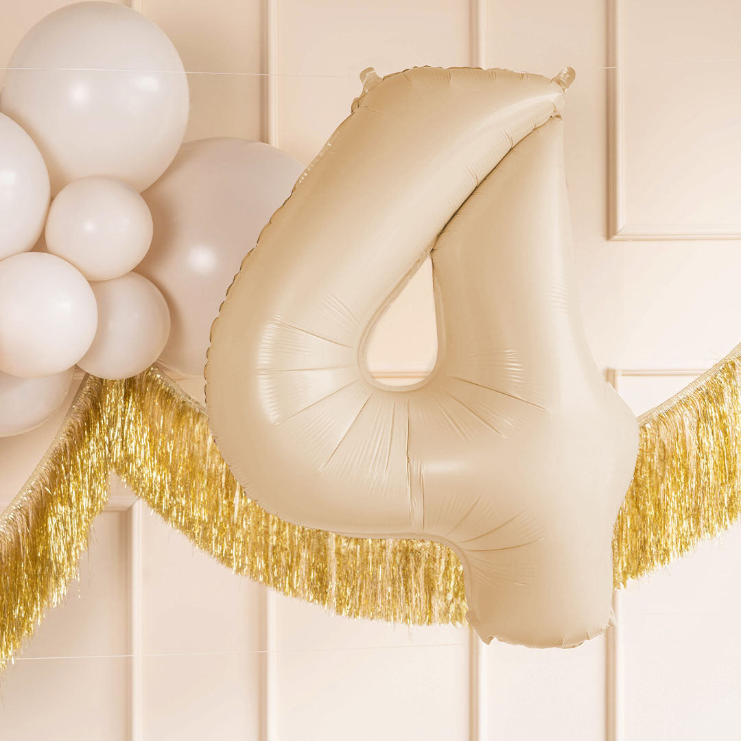 Partydeco cijferballon 4 in beige kleur als onderdeel van een feestdecoratie met witte ballonnen en gouden slingers.