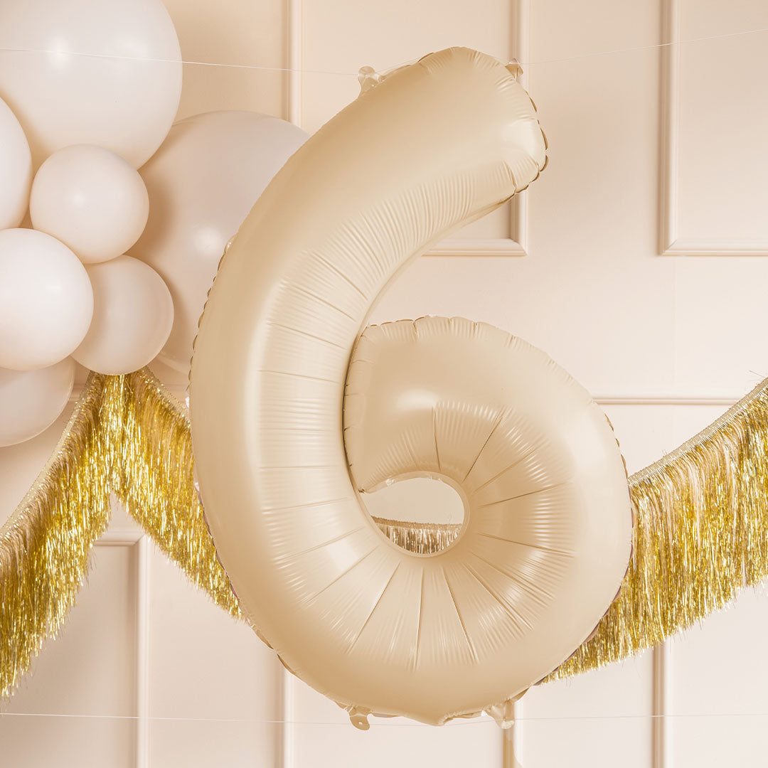 Partydeco beige cijferballon 6 hangend tussen witte ballonnen en een gouden slinger.