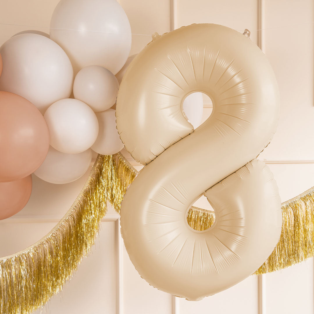 partydeco beige cijferballon 8 hangend tussen witte en roze ballonnen en gouden slingers.