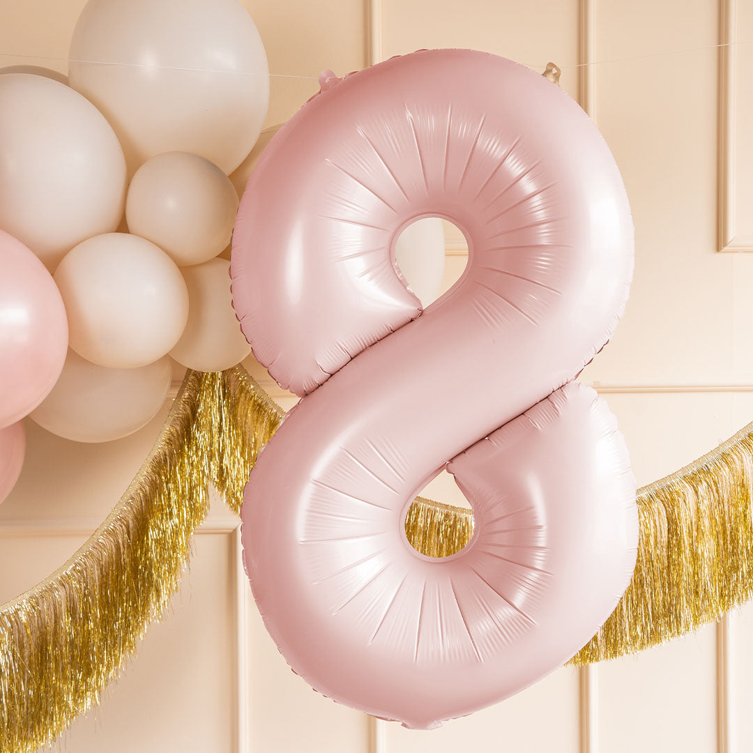 Lichtroze cijferballon 8 hangt in een feestelijke setting met witte ballonnen en een gouden slinger.