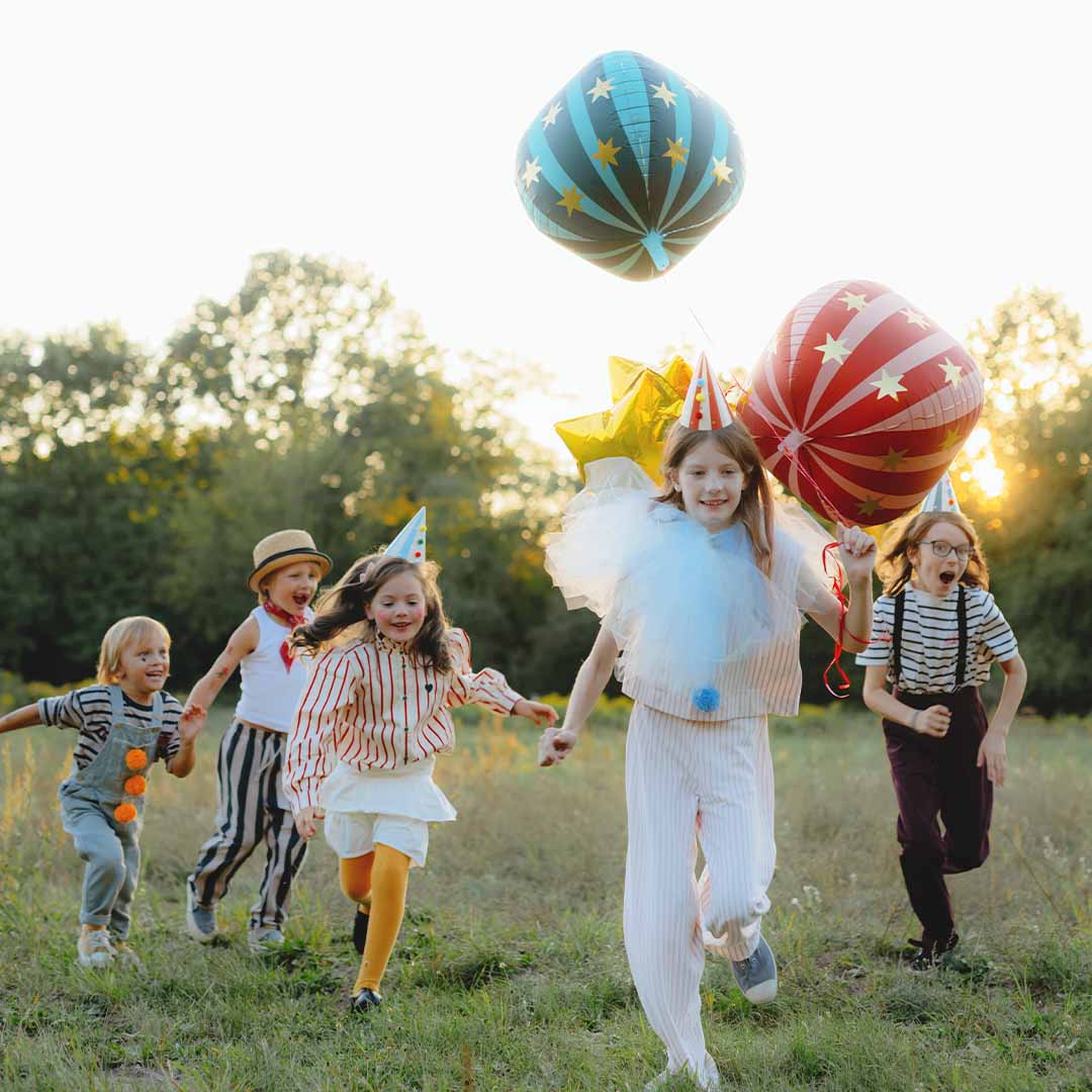 Vijf kinderen rennen door een veld met feestelijke folieballonnen.