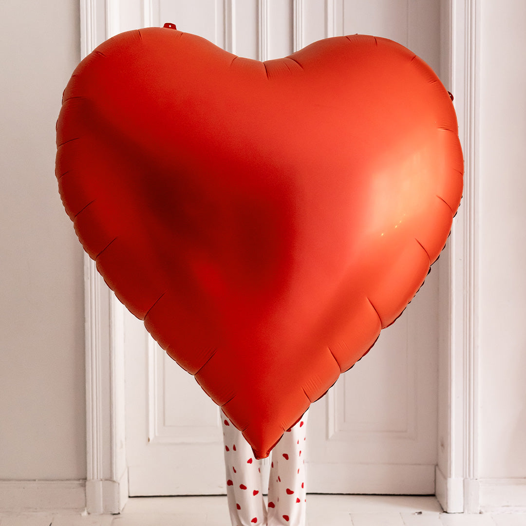 Grote Partydeco rode hartvormige folieballon voor een persoon, staand voor een witte deur.