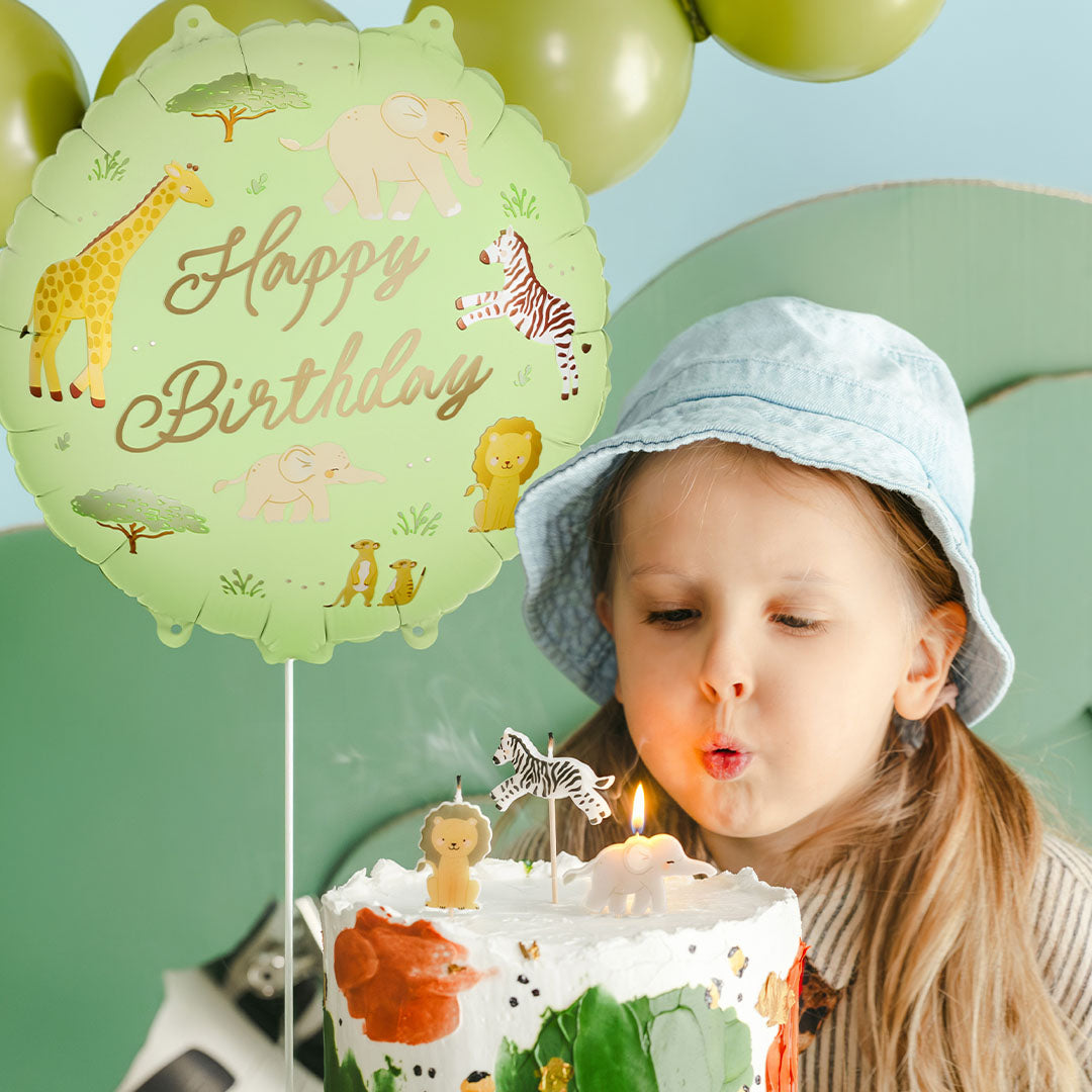 Een meisje blaast kaarsjes uit op een verjaardagstaart, met de partydeco safari 'Happy Birthday' folieballon op de achtergrond.