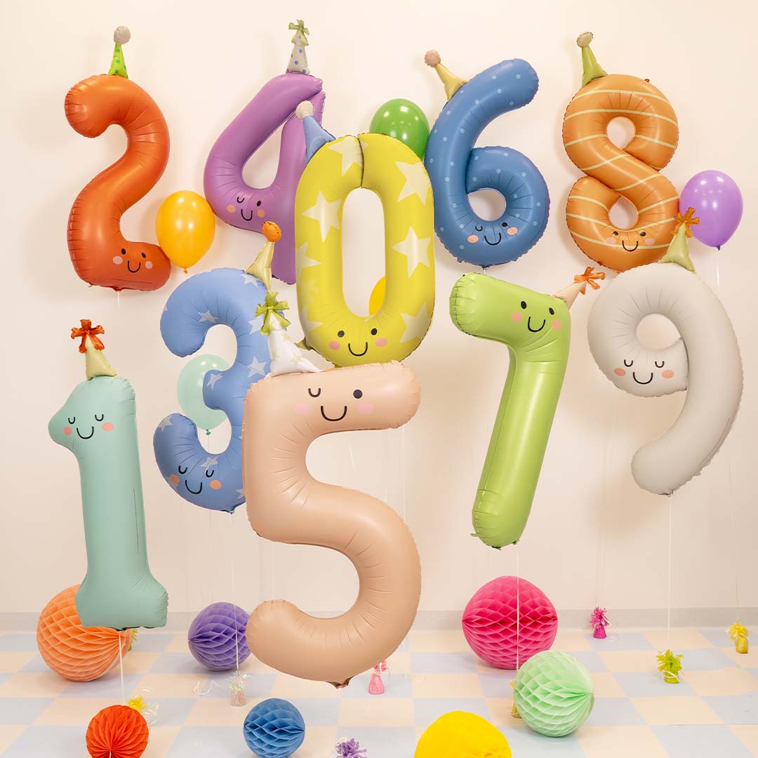 Collectie Partydeco cijferballonnen in verschillende kleuren en nummers, met gezichtjes en feesthoedjes, in een feestelijke setting.