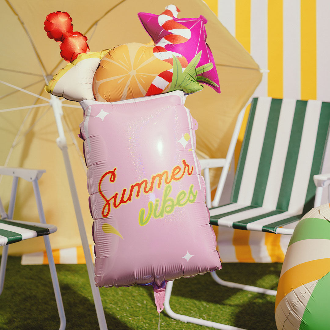 PartyDeco folieballon in de vorm van een roze cocktailglas met fruit, zwevend in een zomerse setting.