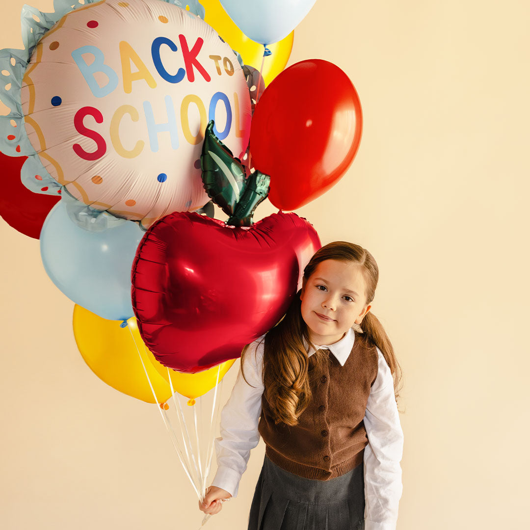 Een meisje houdt een bos ballonnen vast, waaronder de PartyDeco "BACK TO SCHOOL" folieballon en een rode appelballon.
