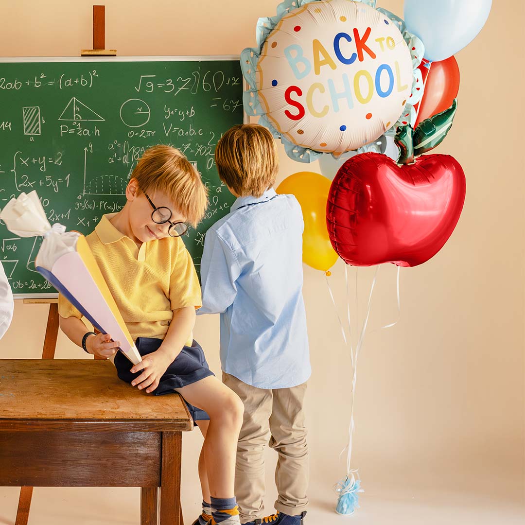 Twee jongens in een klaslokaal met een schoolbord en een bos ballonnen, waaronder de PartyDeco "BACK TO SCHOOL" folieballon.