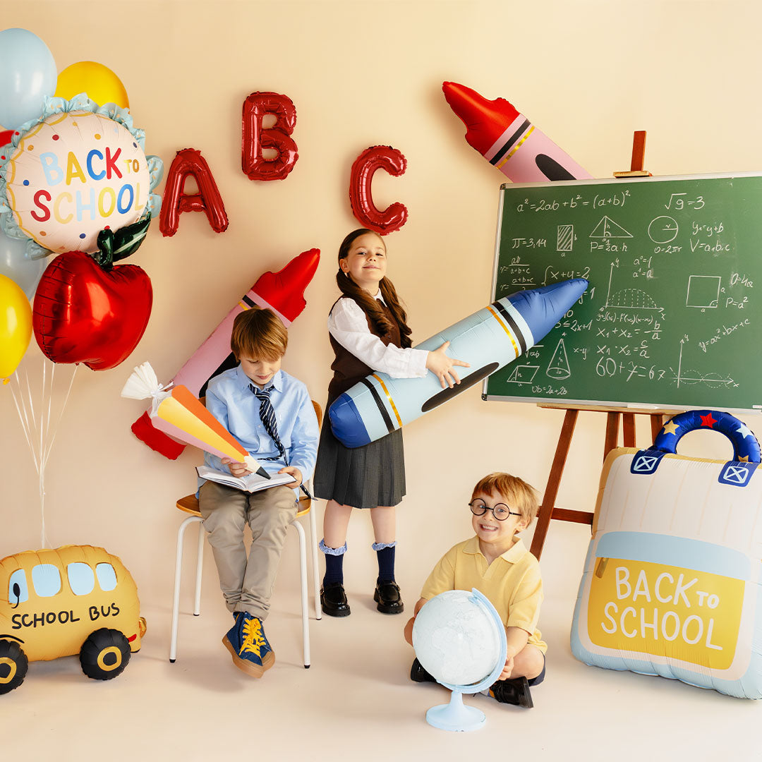 Drie kinderen in een schoolsetting met diverse Partydeco schoolthema feestdecoraties, waaronder de schoolrugzak folieballon.