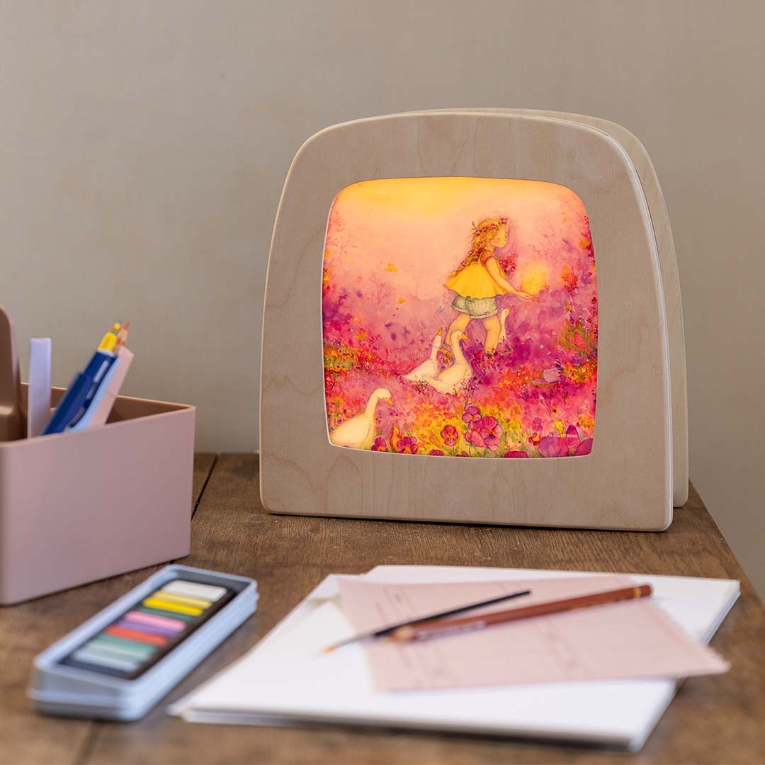 De toverlux toverlamp met de ganzenhoedster illustratie staat verlicht op een houten bureau met tekenbenodigdheden.