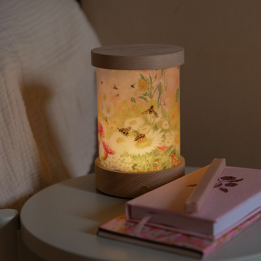 Toverlux lichtkaart voor lantaarn met bloemen en bijen patroon, verlicht op een nachtkastje naast een roze notitieboekje.