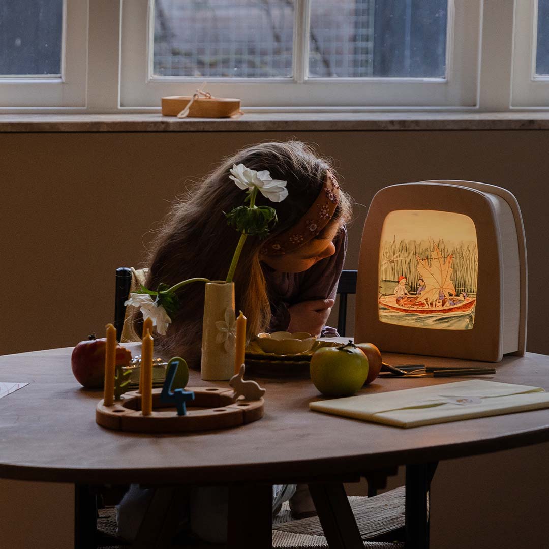 Een kind zit aan tafel naast de verlichte toverlux toverlamp met de toverplaat van de kinderen in een bootje.