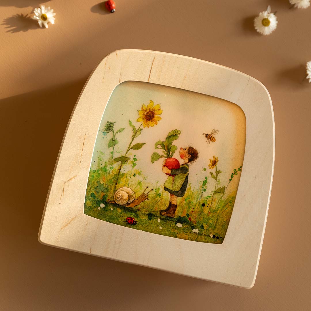 Toverlux toverplaat met houten frame en illustratie van een kind met radijs en slak, schuin gefotografeerd op een bruine ondergrond.