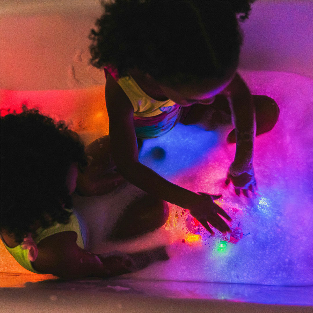 Twee kinderen spelen in een bad vol schuim, verlicht door de kleurrijke badspeelgoedblokjes.