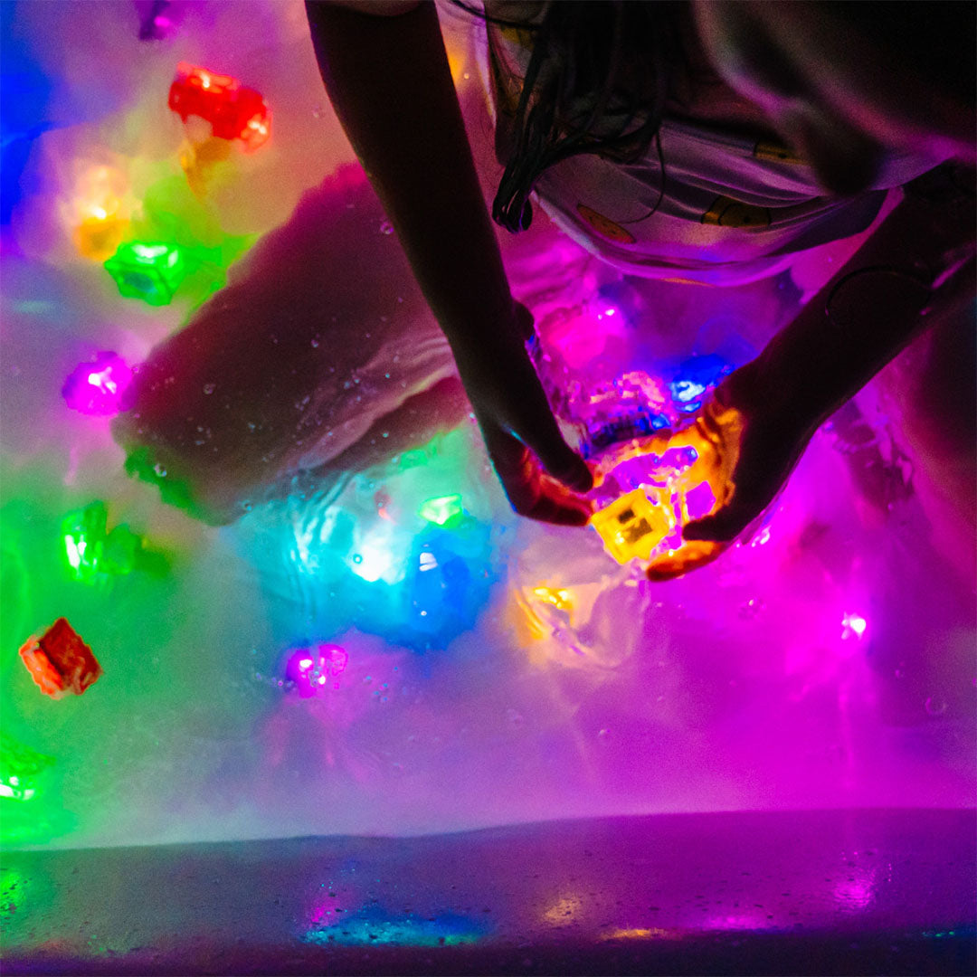 Kinderhanden spelen met meerdere oplichtende badspeelgoedblokjes in een bad met gekleurd water.